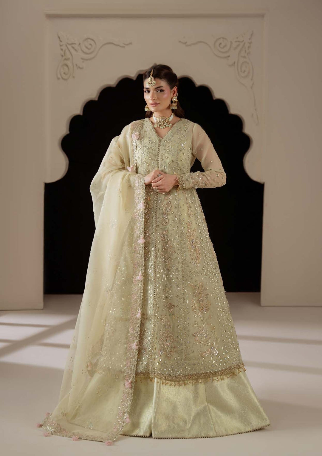 Reverie full length in an arched doorway: a pale champagne long shirt with a sheer dupatta and blush tassels