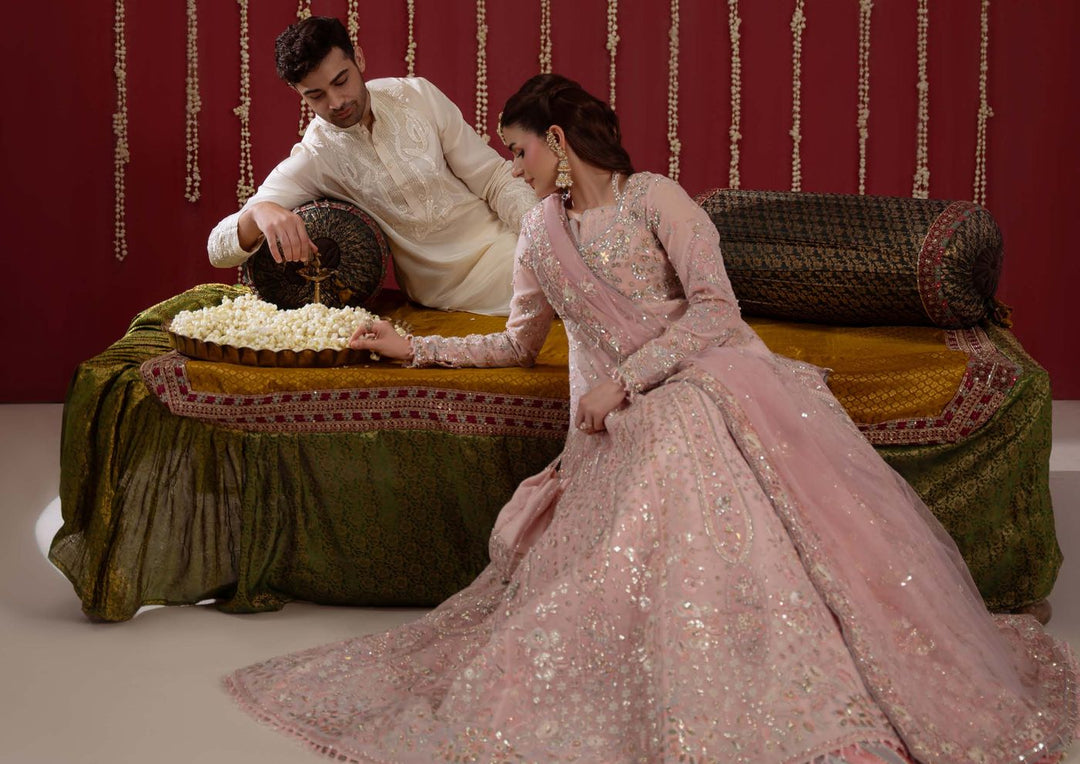 A wide shot of the model and a man in cream seated on a divan with a bowl of flowers