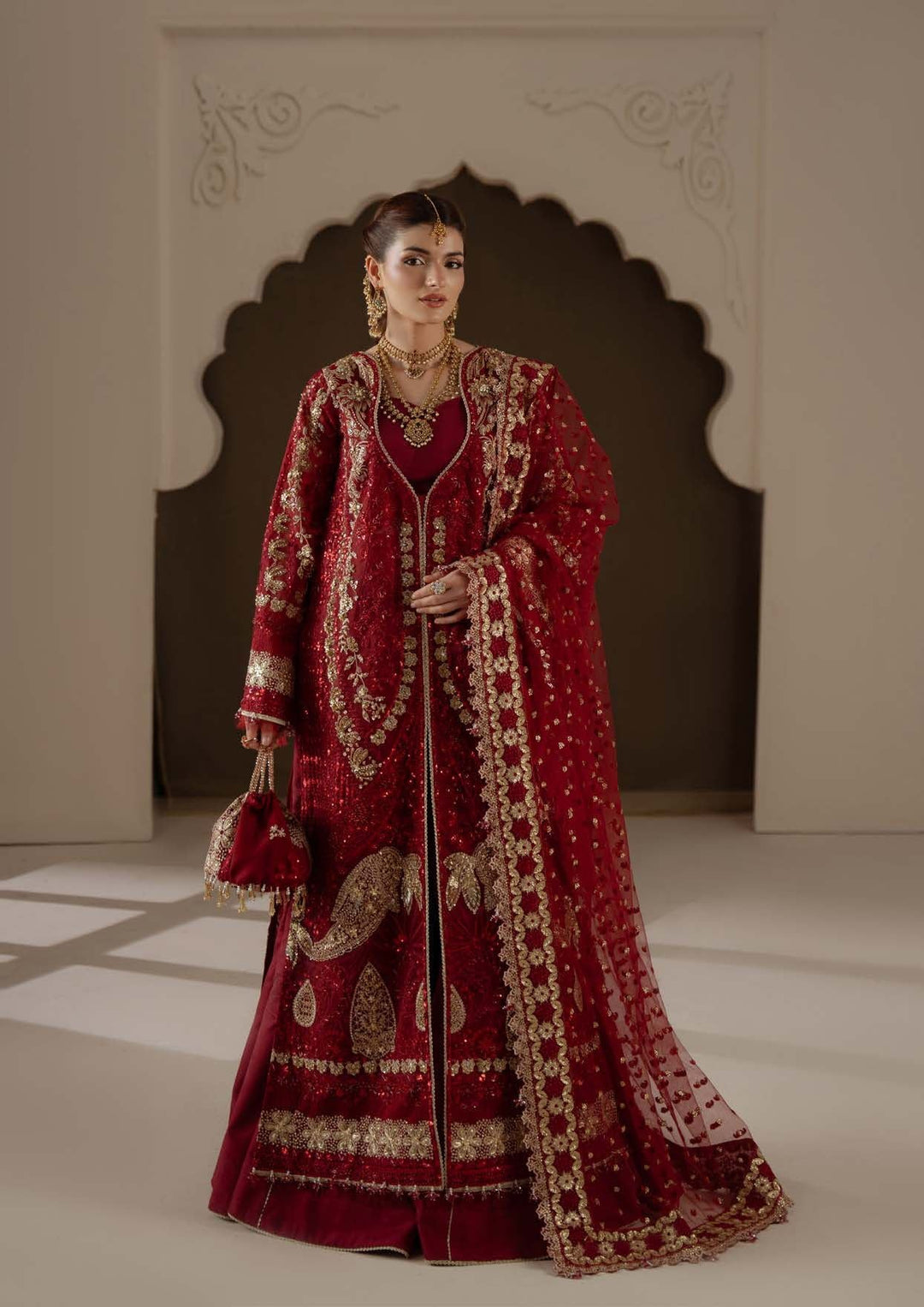 Amour in wine red with gold borders, standing full length in an arched doorway
