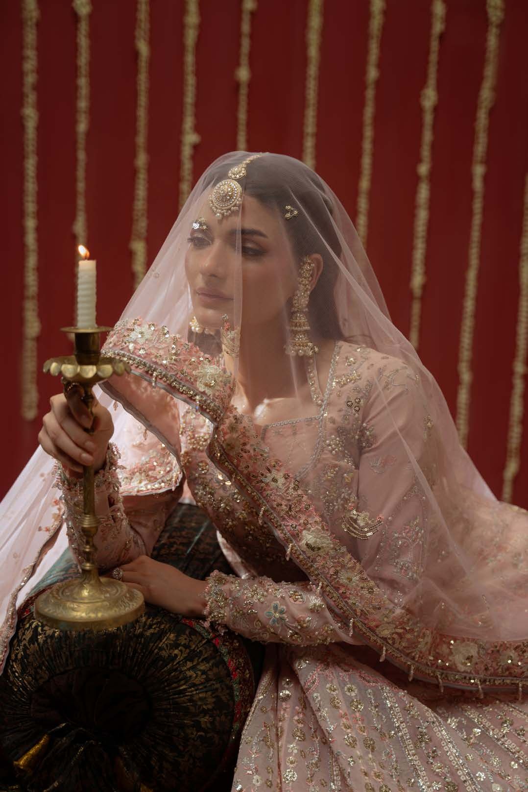 The model veiled in a sheer blush dupatta, holding a brass candle stand